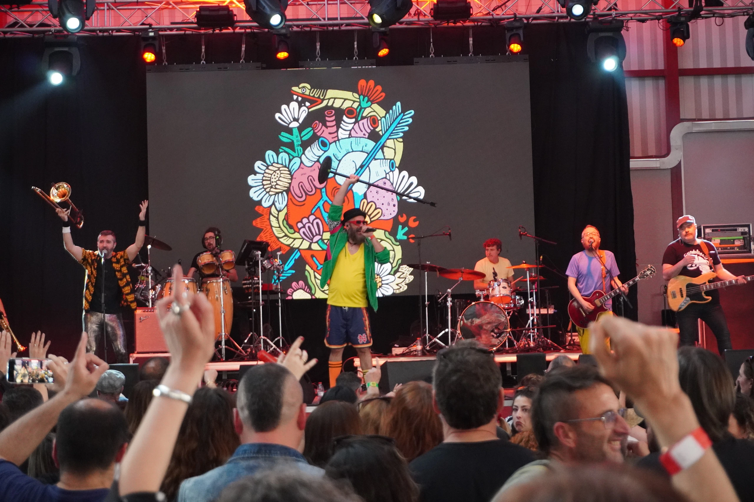 Banda tocando en directo sobre un escenario iluminado frente a un público entregado, capturando la energía de la música en vivo del festival +Espárrago Music and Sound.