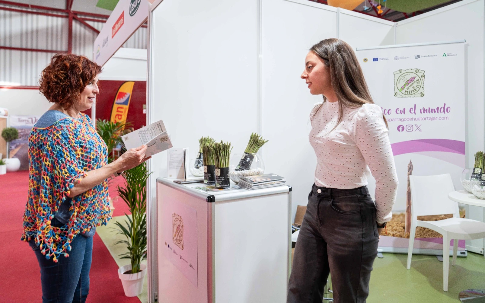 Grupo de autoridades, representantes del sector y la mascota con forma de espárrago posando en el stand de la IGP Espárrago de Huétor Tájar durante la III Feria Gastronómica.